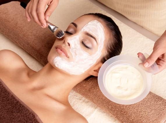 Spa therapy for young woman receiving facial mask at beauty salon - indoors